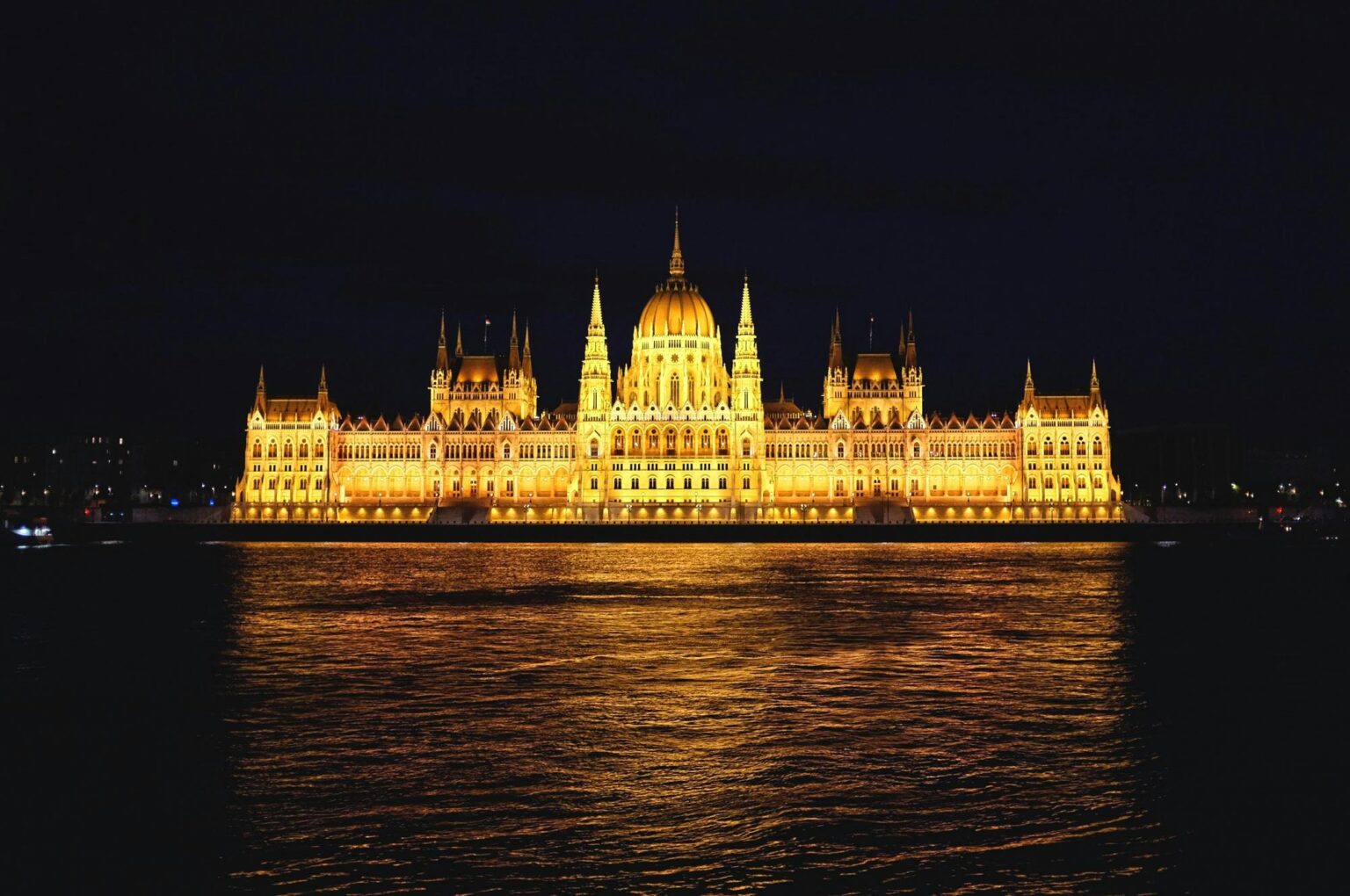 Illuminated Hungarian Parliament Building at night overlooking the Danube River in Budapest.
